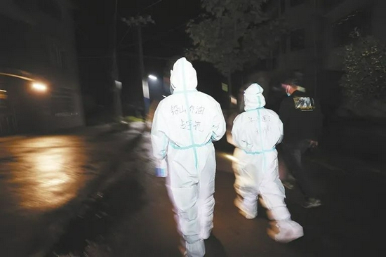 11月2日晚，铅山县虹桥乡，00后志愿者占宇航（左）和医护人员上门为老人进行核酸采样。他的防护服背后写着“铅山，加油！”