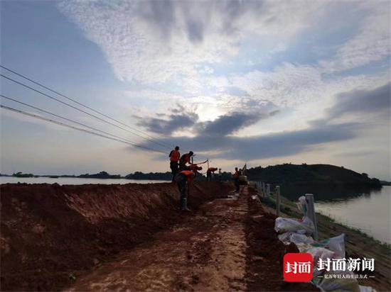阻隔在洪水(左)与水库(右)之间的堤坝,被村民视为“第二道防线”。 武警官兵正在帮忙增加沙袋,加固、增高堤坝。