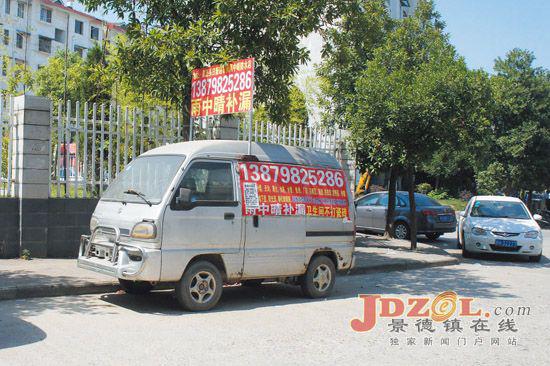 在梨树园小学围栏北面,一辆银灰色微型车上贴满补漏广告