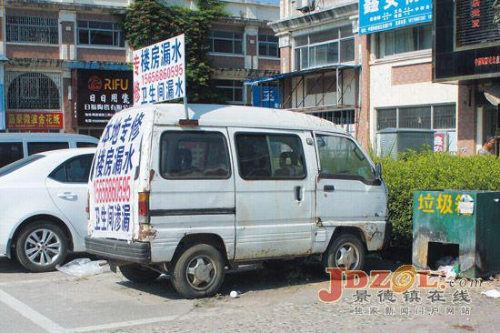 一辆早该报废的白色微型车上贴有专修房屋漏水广告