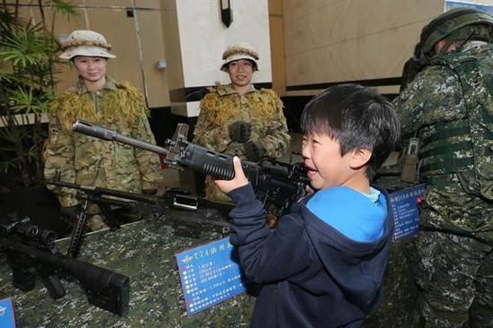 小同伙兴趣勃勃地捧起现场静态展示的特战小组兵器(图片来源:台湾《中时电子报》)