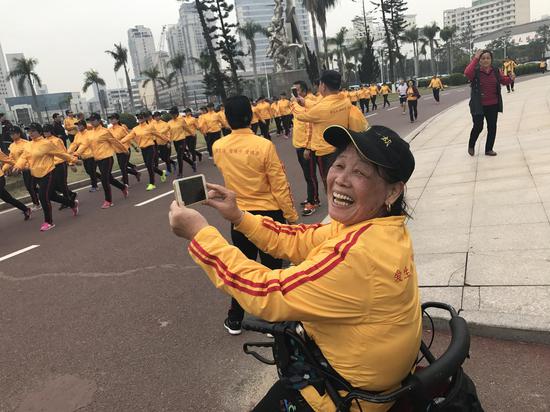 68岁的熊祖永高兴地给队友们拍视频。原来她因车祸下肢失去知觉,二十多年不能行走。去年开始跟借助轮椅跟大家一起锻炼,现在但她每天都能走6000-8000步。