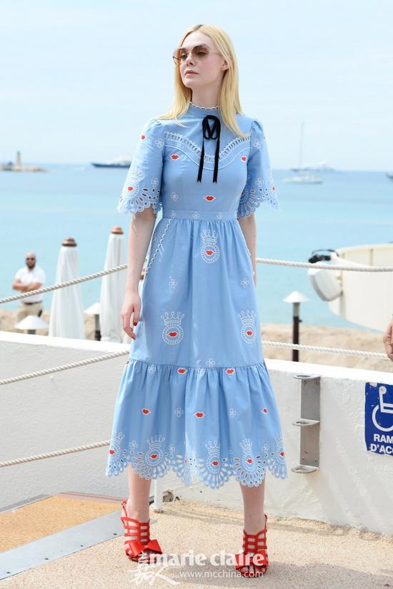 艾丽-范宁（Elle Fanning）街拍。她身穿天蓝色红唇刺绣镂空连身裙，脚踩红色蝴蝶结镂空高跟凉鞋。