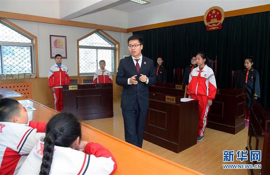 在河北省石家庄市建胜路小学举办的校园模拟法庭现场，石家庄市桥西区检察院检察官为学生们讲解庭审程序（2017年12月4日摄）。新华社发（章朔 摄）