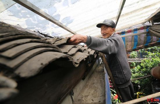 陈德君爬梯子维修屋顶瓦片。
