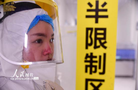 2020年1月31日,重庆市璧山区人民医院感染科隔离病房的90后护士匡艳,换好防护服准备走进病房,脸上满是被口罩勒出的伤痕。胡悦建/人民图片