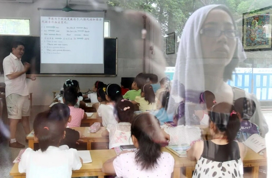 2011年7月7日,江苏省南通市,一名家长头顶毛巾站在教室外隔窗观望正在上“班”的孩子。图/视觉中国