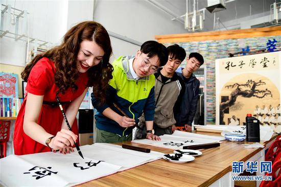 2018年5月3日，在中国石油大学（华东）大学生活动中心，哈萨克斯坦留学生珍珠（左一）在翰墨飘香书画社校友的指导下用毛笔在宣纸上书写。新华社记者 郭绪雷 摄