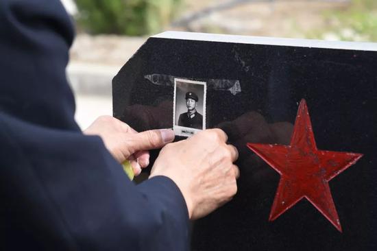 魏聚增的哥哥在墓碑上贴上烈士生前照片。受访者供图