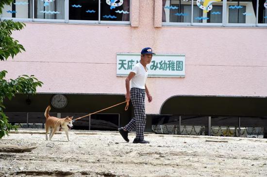 7月11日，在日本广岛吴市天应町地区，一名居民走过被泥石流部分淹没的幼儿园。新华社记者马平摄