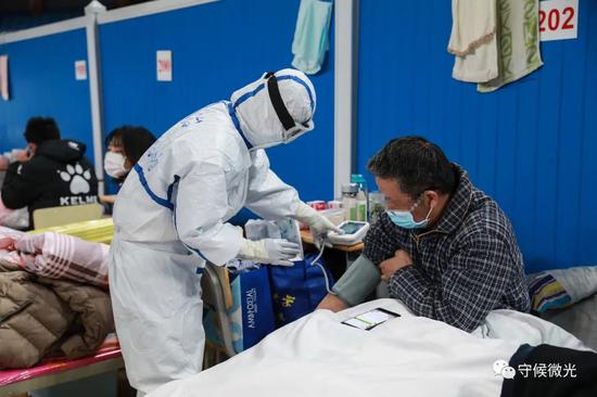 2月21日,武汉市洪山体育馆方舱医院A区内,医护人员在给病患丈量血压。中青报·中青网见习记者 鲁冲/摄
