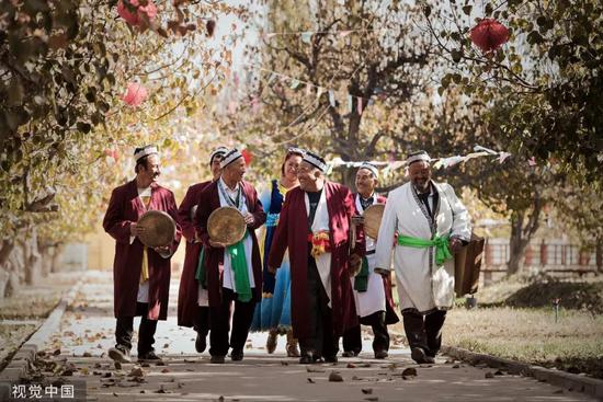 ▲资料图片：2018年10月23日，新疆喀什，一群手持乐器的维吾尔族刀郎木卡姆传承艺人，正有说有笑地由果园深处走来。