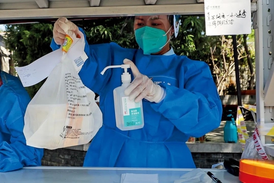 6月1日,北京市西城区鼓楼西大街相关区域因疫情采取封、管控措施,外卖快递车辆无法进入,地安门邮局在鼓楼西大街东口和西口设立快递中转站。社区志愿者接收物品后对外包装进行消杀。摄影/本刊记者 贾天勇
