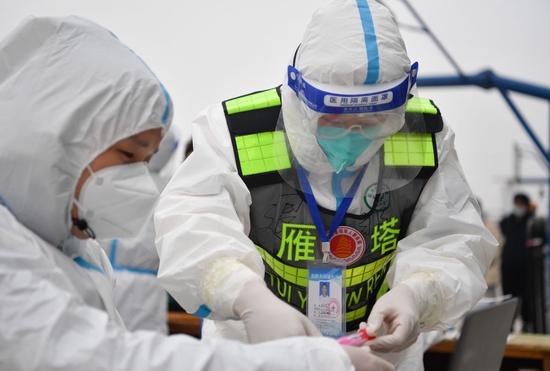 ↑1月7日，西安市雁塔区退役军人志愿突击队队员邹浩东（右）在一处核酸检测点与工作人员交接核酸检测样本。