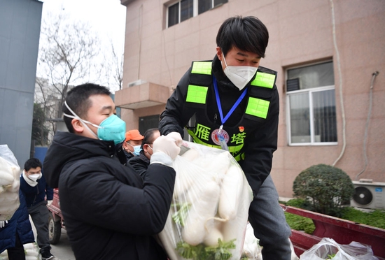 ↑1月6日，西安市雁塔区退役军人志愿突击队队员侯磊（右）协助社区工作人员搬运物资。