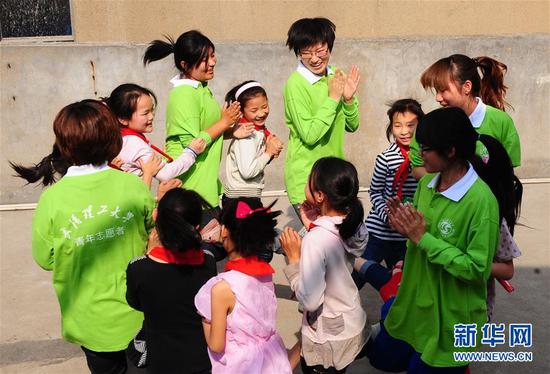 2011年4月28日，武汉理工大学研二学生郎坤和农民工子弟学校武汉凌智小学的孩子们一起在屋顶平台上做游戏。新华社记者 程敏 摄