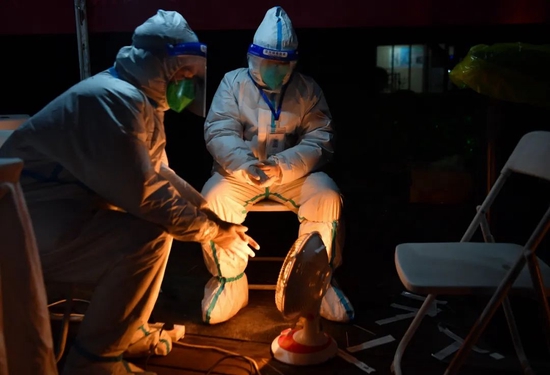 2021年12月31日，在西安某小区内，两名志愿者在核酸检测工作结束后取暖（新华社记者 张博文 摄）