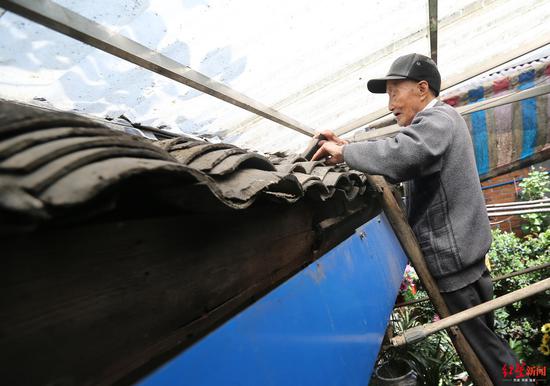 陈德君爬梯子维修屋顶瓦片。