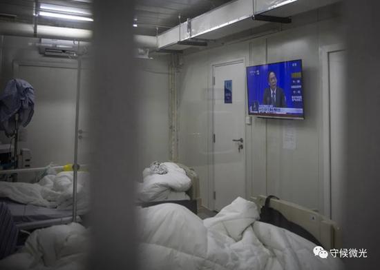 2月21日,武汉火神山医院感染八科,新冠肺炎患者在病房内的电视上收看当天在北京举办的国务院联防联控机制新闻发布会直播。中青报·中青网记者李峥苨/摄