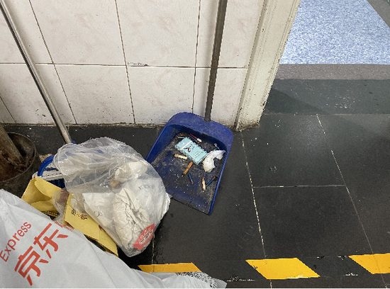 西单明珠商场保洁员的簸箕内有不少烟头。