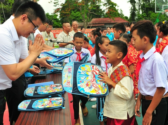 ↑2019年6月1日，在老挝万象，中老友好农冰村小学学生接过中老铁路中国工作人员赠送的文具礼物。