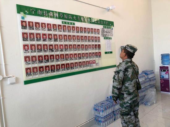 宁南扑火队的营地内，一名队员正在看展板上的照片。新京报记者 王翀鹏程 摄
