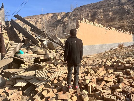 12月20日，一名康吊村村民站在自家倒塌的房屋前。