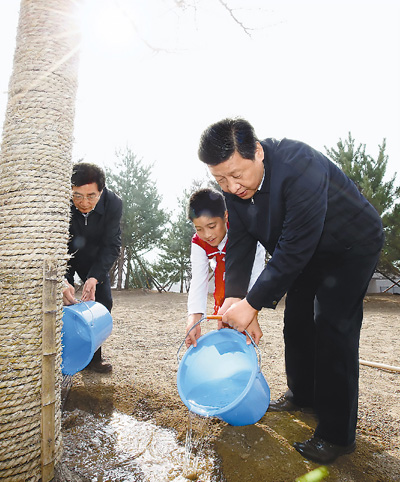 2013年4月2日，习近平同少先队员一起给刚栽下的银杏树浇水。
