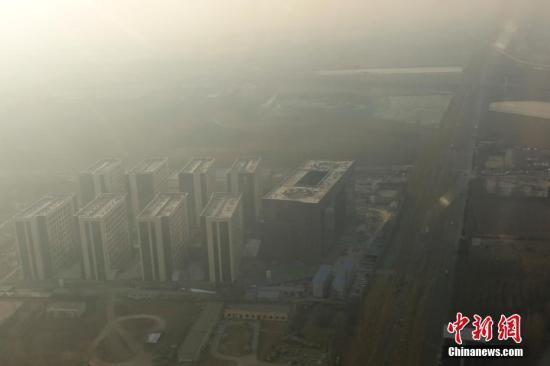  12月16日，透过飞机舷窗俯瞰北京，城市建筑隐在雾霾中。12月15日北京发布今年首个空气重污染红色预警：16日20时，北京市启动空气重污染红色预警。中新社记者 盛佳鹏 摄