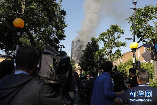 6月14日，在英国伦敦，媒体记者在发生火灾的大楼附近拍摄。