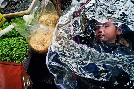 在纽约唐人街,你能买到最新鲜的鱼、肉和蔬菜,也能吃到最正宗的中国菜,图中,菜市场的孩子在菜摊旁熟睡。