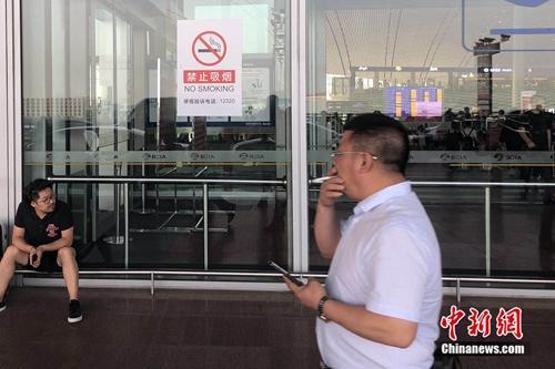 5月25日,一男子在北京首都机场的禁烟标识下吸烟通过。 冷昊阳 摄