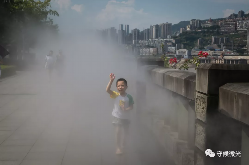 重庆市万州区，一名小朋友在高温中穿过降温水雾。