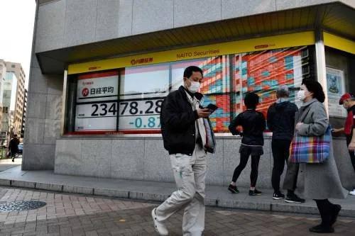 ▲2月21日,在日本东京,路人走过街边的电子股指信息显示屏。新华社/法新