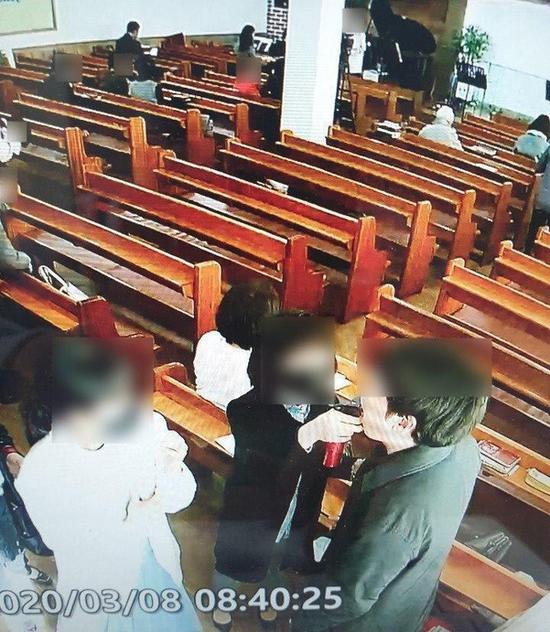 牧师夫人手持喷壶,向教徒嘴里喷盐水。