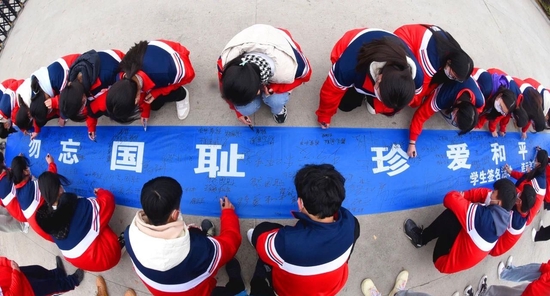 △江苏连云港，高中学生在“勿忘国耻，珍爱和平”条幅上签名。