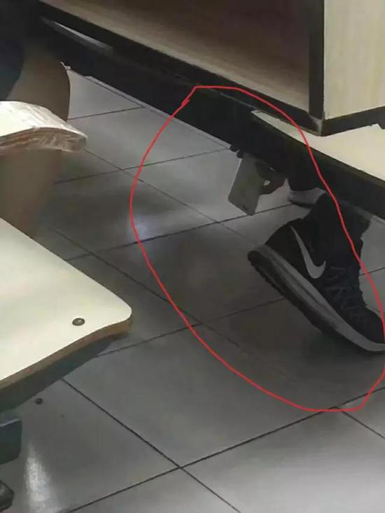 ▲男生以系鞋带的姿势,将手机后置摄像头伸到座位下方,试图偷拍。这一幕被教室内的其他同学当场记录。