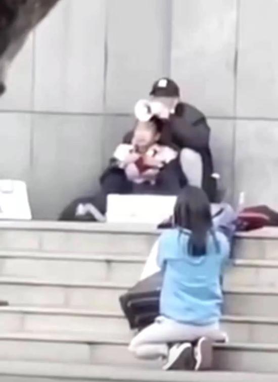  ▲蓝衣女记者跪在台阶上面对劫持者。图/新京报网。