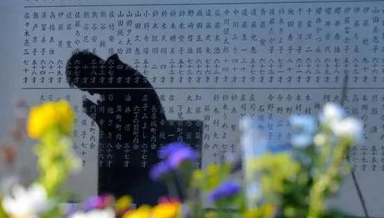 一个男人在日本宫城县仙台市祈祷,他的身影映在一座2011年海啸纪念石碑上。
