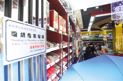 7月4日，深圳市坪山区马峦市场监管所执法人员在万众百货的烟酒摊位前执法。本版图片/深圳市卫生计生委