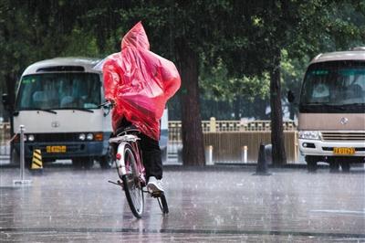 昨日上午，北京西單附近，市民雨中邊騎車邊整理雨衣。新京報實習生 陳婉婷 攝