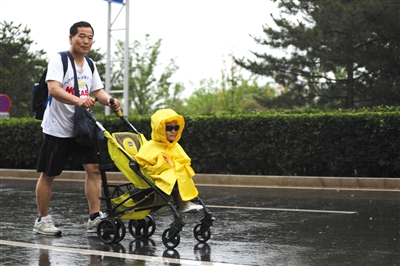 5月26日,天辰東路,一位市民冒雨推着童車前行,車上坐着“全副武裝”的小朋友。新京報記者 王飛 攝