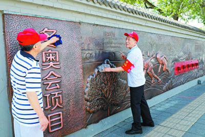 昨天，石景山区古城街道“老街坊”志愿者正在擦拭新建成的冬奥主题浮雕墙。冬奥浮雕墙全长112米，高1.6米，采用铜板浮雕的形式，展示了短道速滑、速度滑冰、花样滑冰、冰球、冰壶等15个冬奥比赛项目。本报记者 吴镝摄