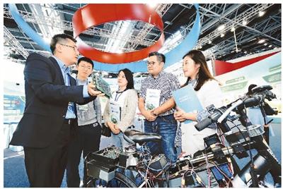 10月8日,北京一家企业工作人员(左一)正在2018全国双创周北京会场展示自主研发的类脑芯片,它具有高计算力、高多任务并行度和较低功耗等优点。本报记者 贺 勇摄