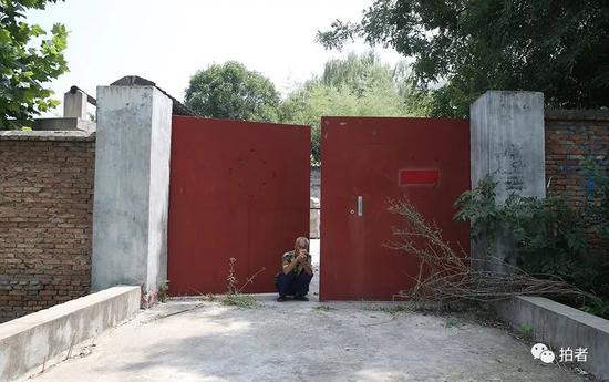 ▲“陈路别墅”的大门，从外观看极为普通的简易红色铁大门，别墅看门的老人蹲在大门口。