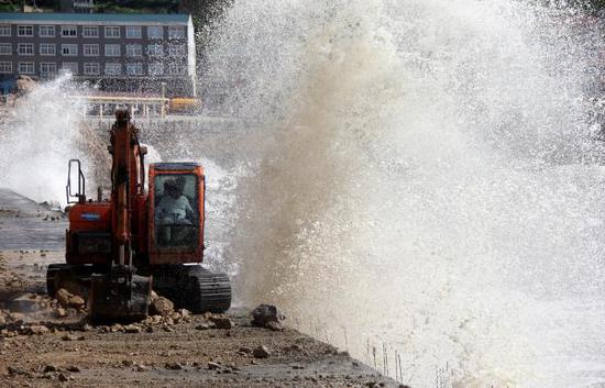 2018年7月10日，浙江温岭市石塘镇金沙滩海域，原本平静的潮水掀起巨浪，将一辆正在加固海塘堤坝作业的挖掘机淋湿。 东方IC 图