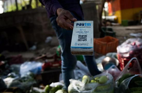 2018-06-22,在印度新德里街头,一名蔬菜摊主手持Paytm二维码接受电子支付。印度Paytm在支付宝母公司蚂蚁金服的支持下,已经成为印度最大的移动支付平台。新华社记者毕晓洋摄