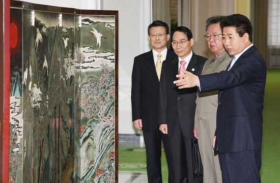 2018-08-16,朝鲜平壤,时任韩国总统卢武铉(右一)与时任朝鲜最高领导人金正日(右二)正在观看卢武铉赠送的屏风。