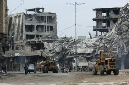 1月4日，在伊拉克摩苏尔，两辆推土机从街头废墟旁经过。新华社发（哈利勒·达伍德摄）