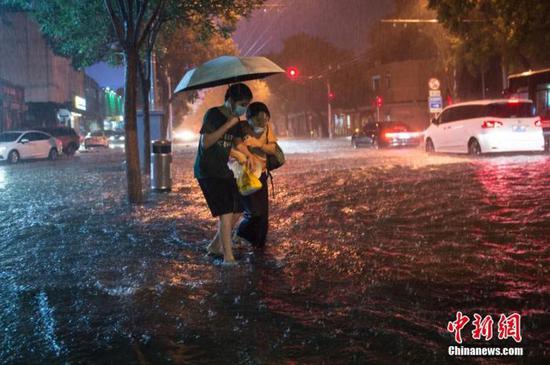 资料图:8月9日晚,北京市民冒雨涉水出行。当日,北京气象台发布18时至23时降水量(毫米):全市平均17.9,城区平均28.1。 中新社记者 田雨昊 摄